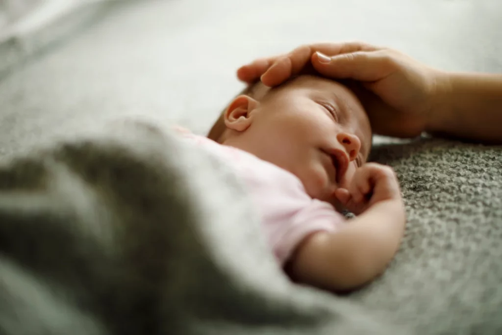schlafendes Baby, Hand streichelt sanft den Kopf