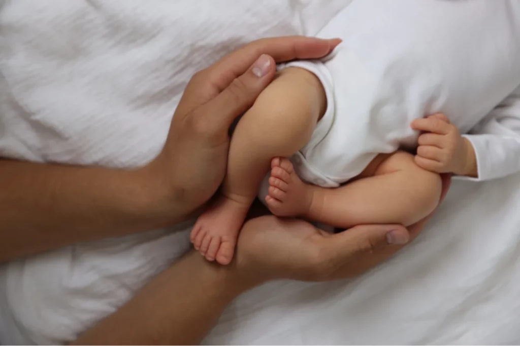 Baby-Füße sanft in Elternhänden gehalten, neutral in Weiß gekleidet