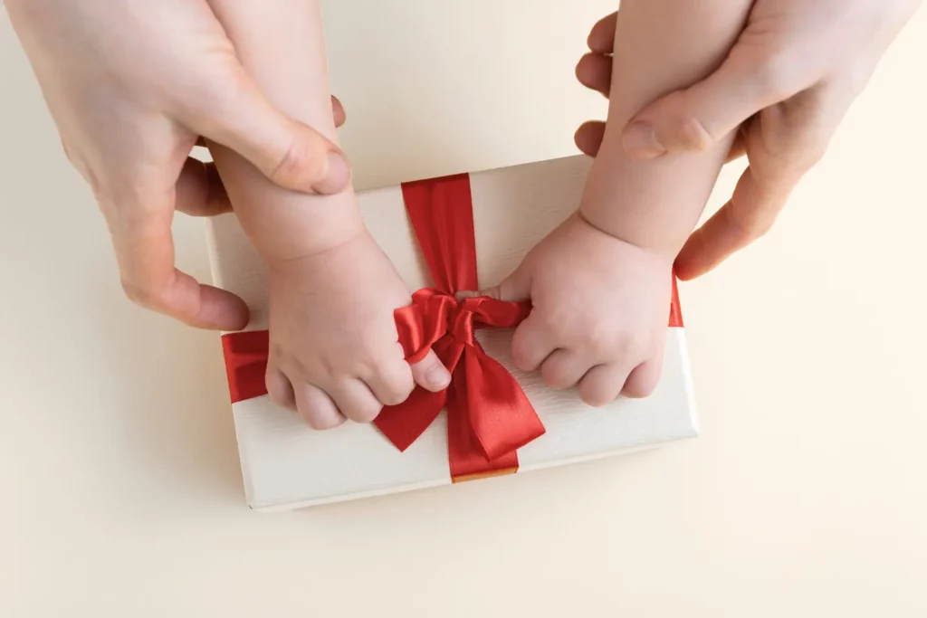 Hände von Baby und Mutter halten Geschenk mit Schleife