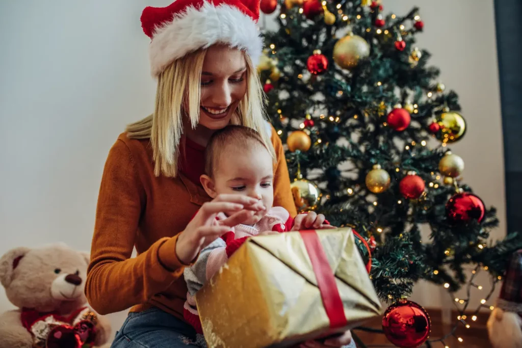 Mama mit Weihnachtsmütze und Baby packen gemeinsam ein goldenes Geschenk aus