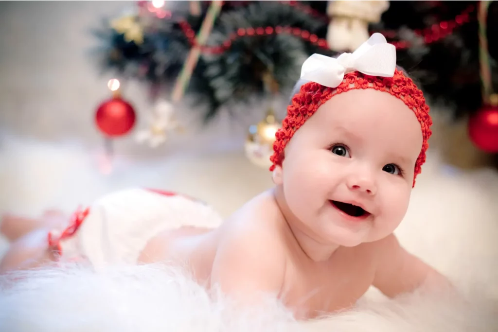 Lächelndes Baby mit rotem Haarband liegt auf einem weißen Fell vor dem Weihnachtsbaum