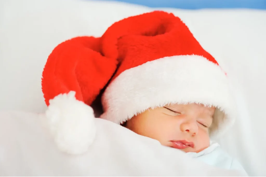 Schlafendes Neugeborenes mit roter Weihnachtsmütze auf einer weißen Decke