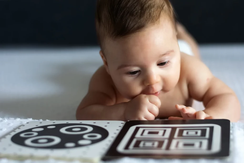 Baby liegt auf dem Bauch und schaut ein Kontrastbuch in Schwarz und Weiß an