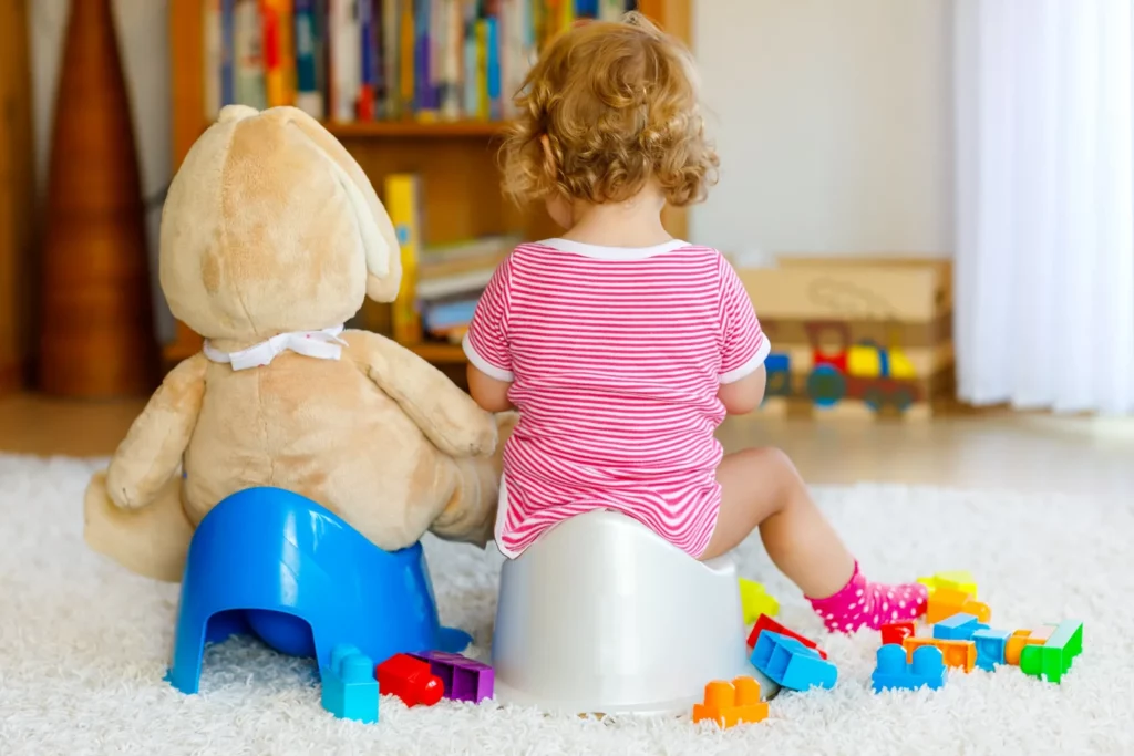 Kleinkind sitzt auf dem Töpfchen neben einem Kuschelhasen vor einem Bücherregal